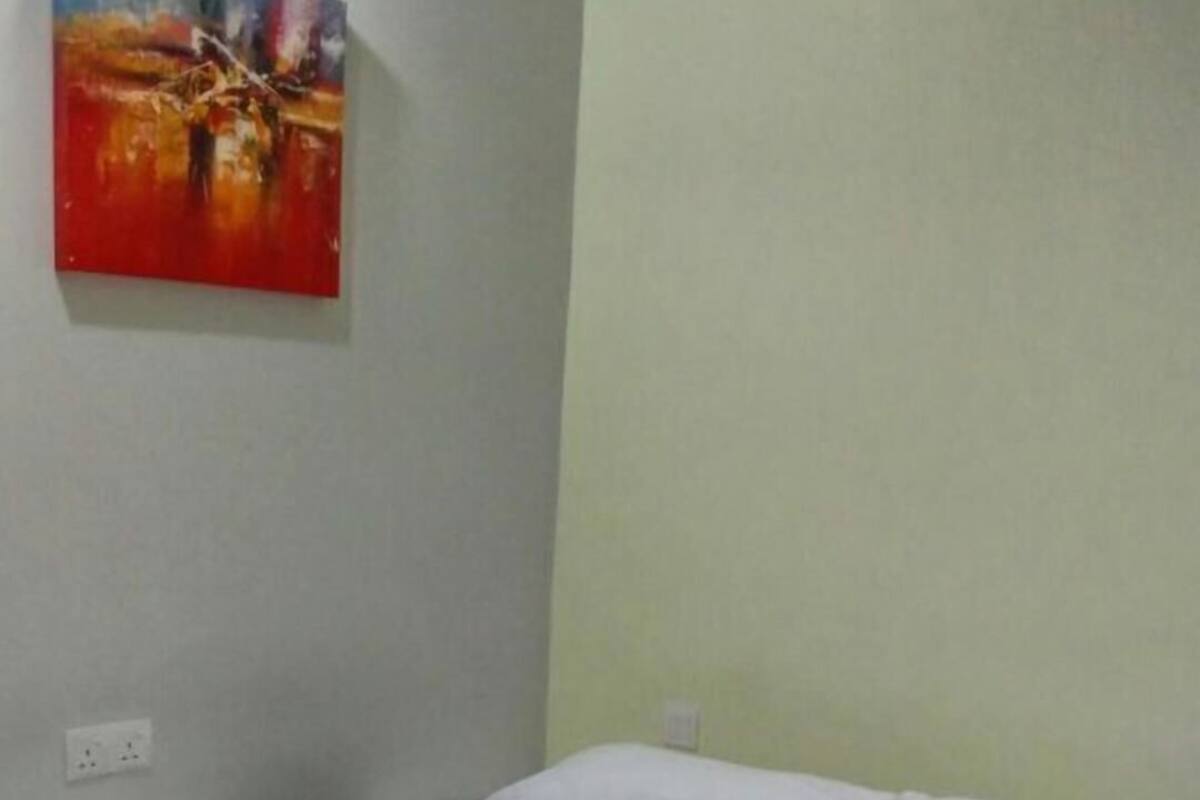 A single bed with white bedding, a green bedspread, and a painting on the wall.