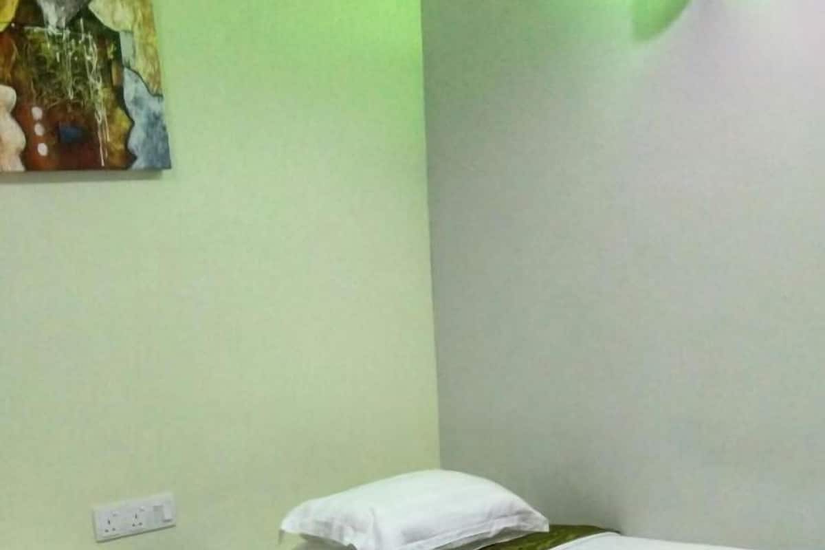 A hotel room with three single beds, each with white linens and a green blanket.