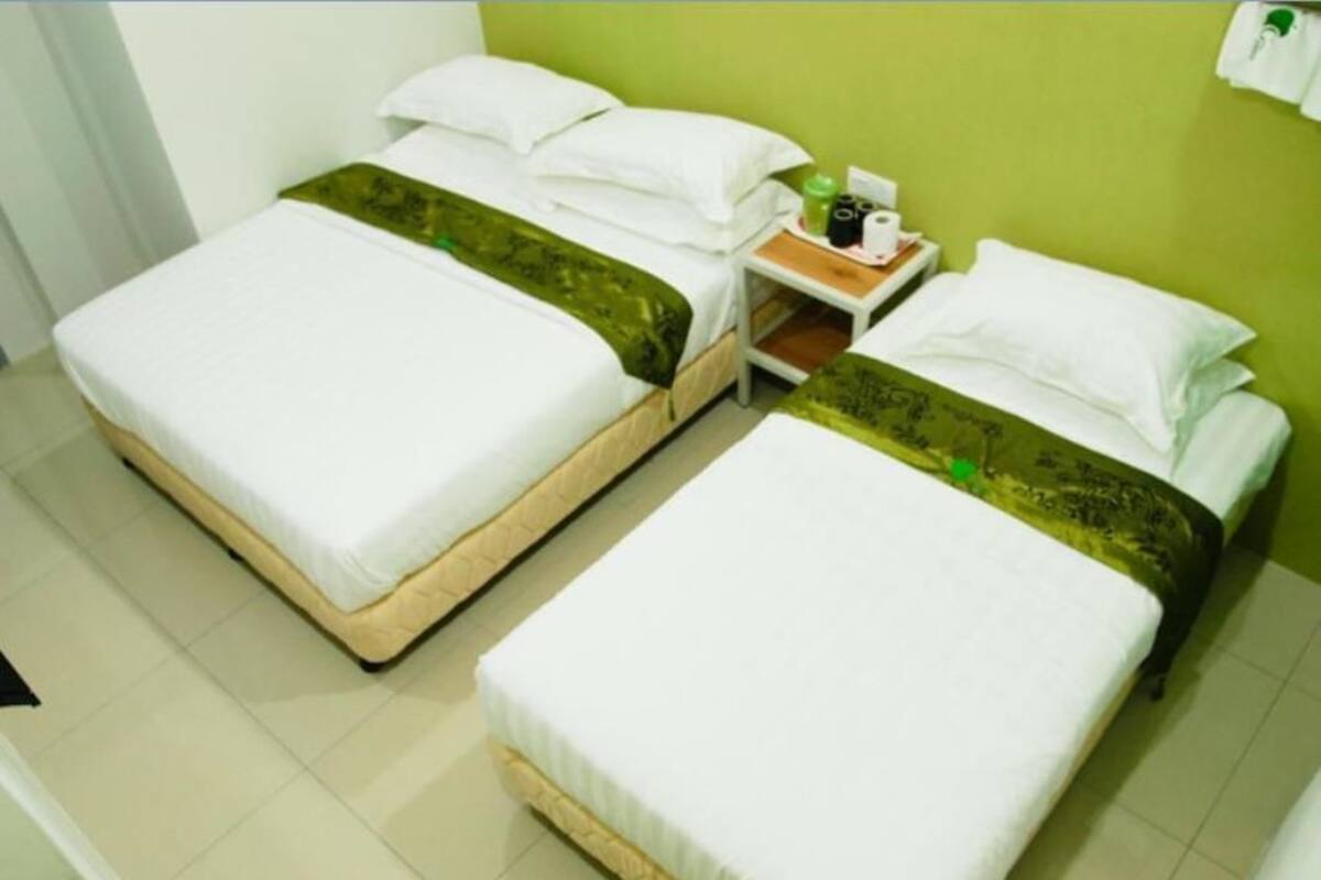 A hotel room with two single beds, a nightstand with toiletries, and a green wall.