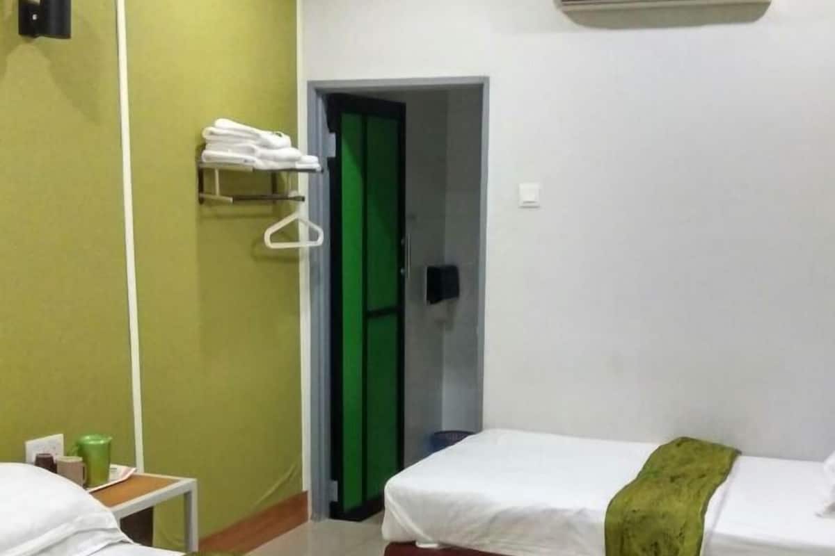 A hotel room with two beds, a green wall, a white door, and an air conditioning unit.