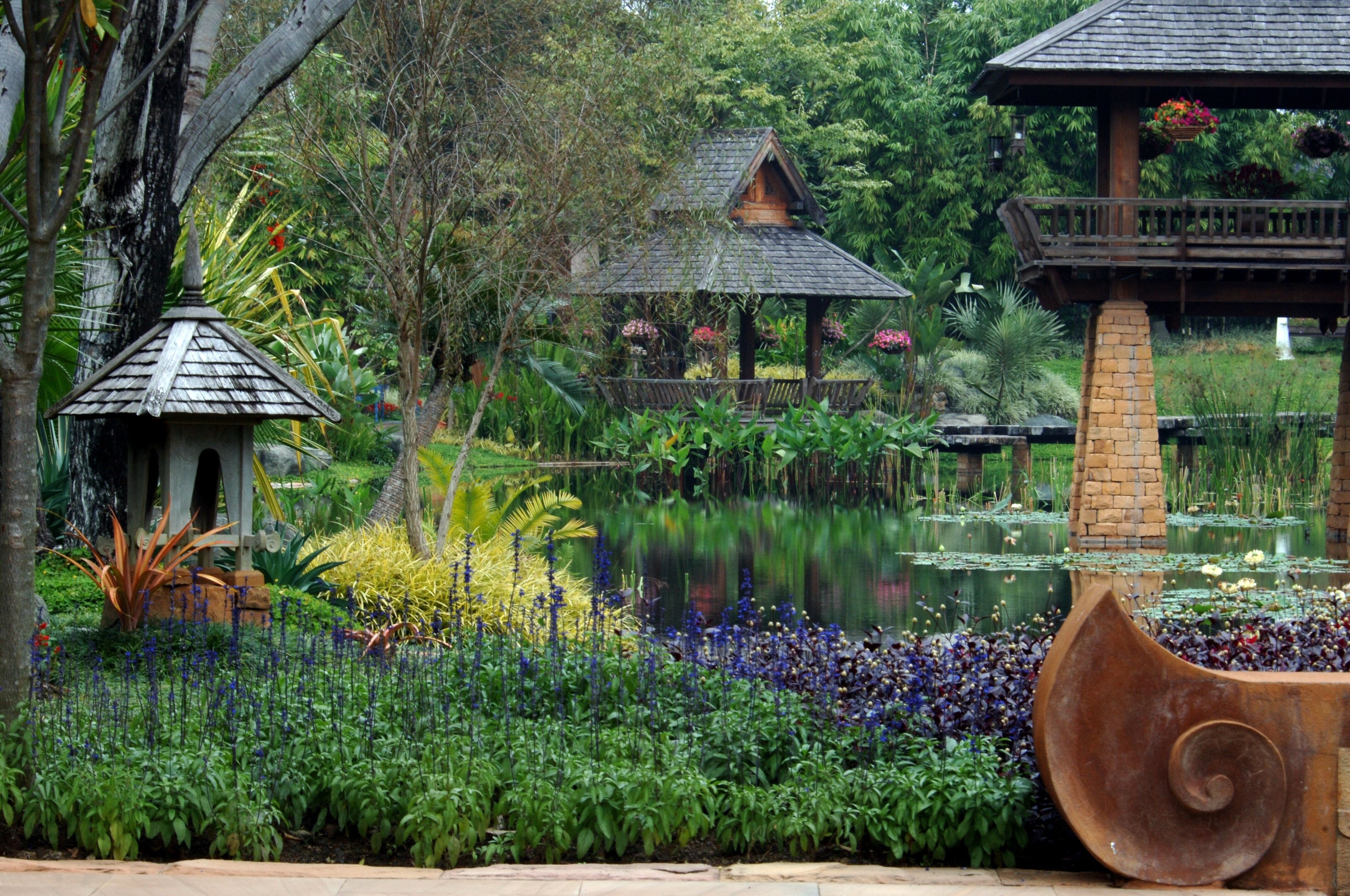 Un jardín con un estanque, un pabellón y una estructura de madera con flores.