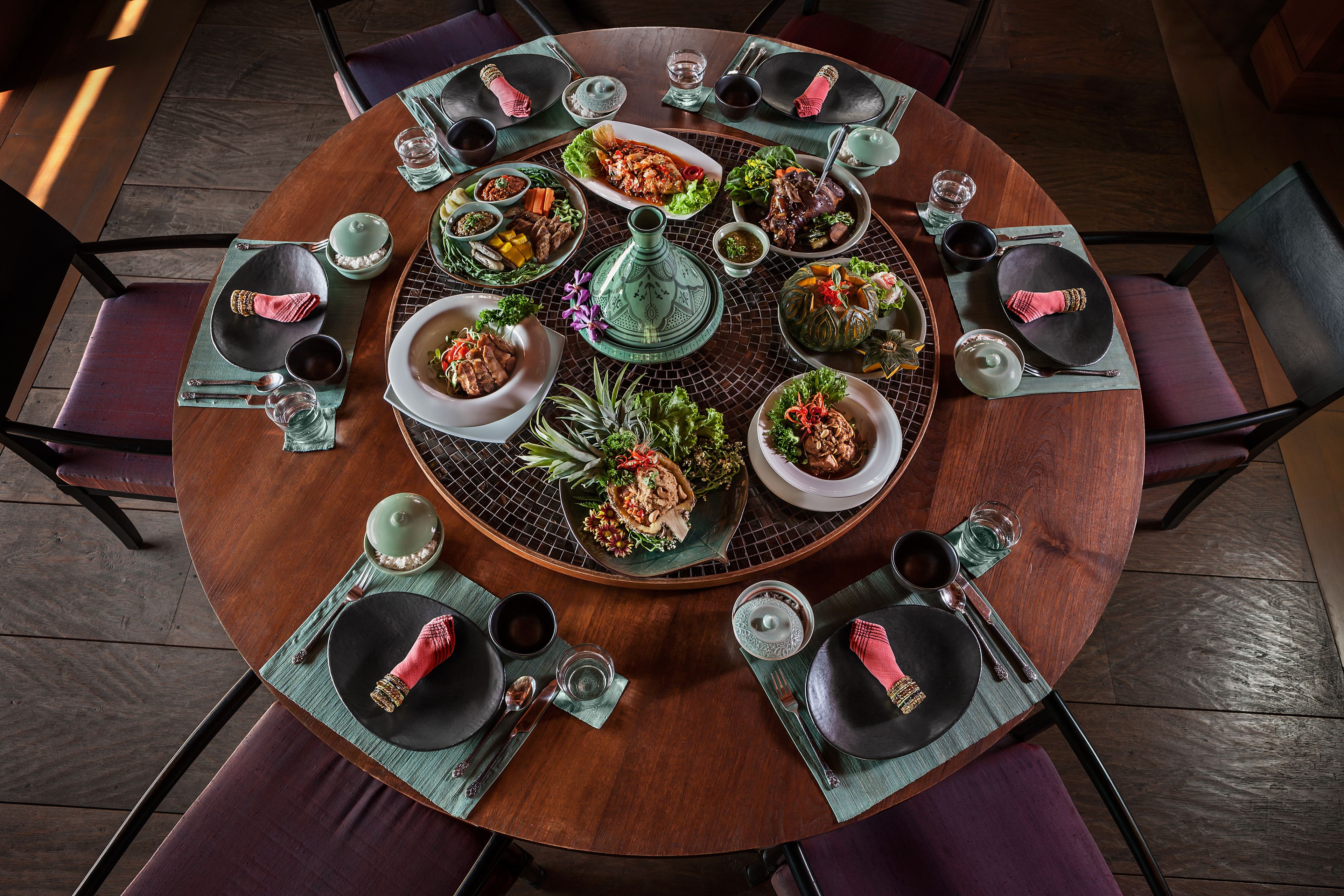 A round dining table with multiple dishes and utensils, surrounded by chairs.