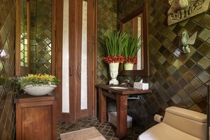 A bathroom with a wooden vanity, a large mirror, a toilet, and a decorative plant. - Howie's Homestay (Mae Rim)