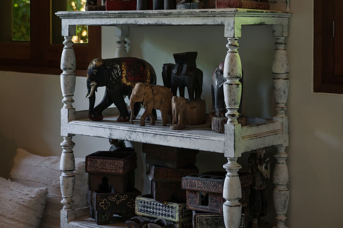A multi-tiered shelf with various cultural artifacts, including figurines and boxes, against a wall with a large painting above.