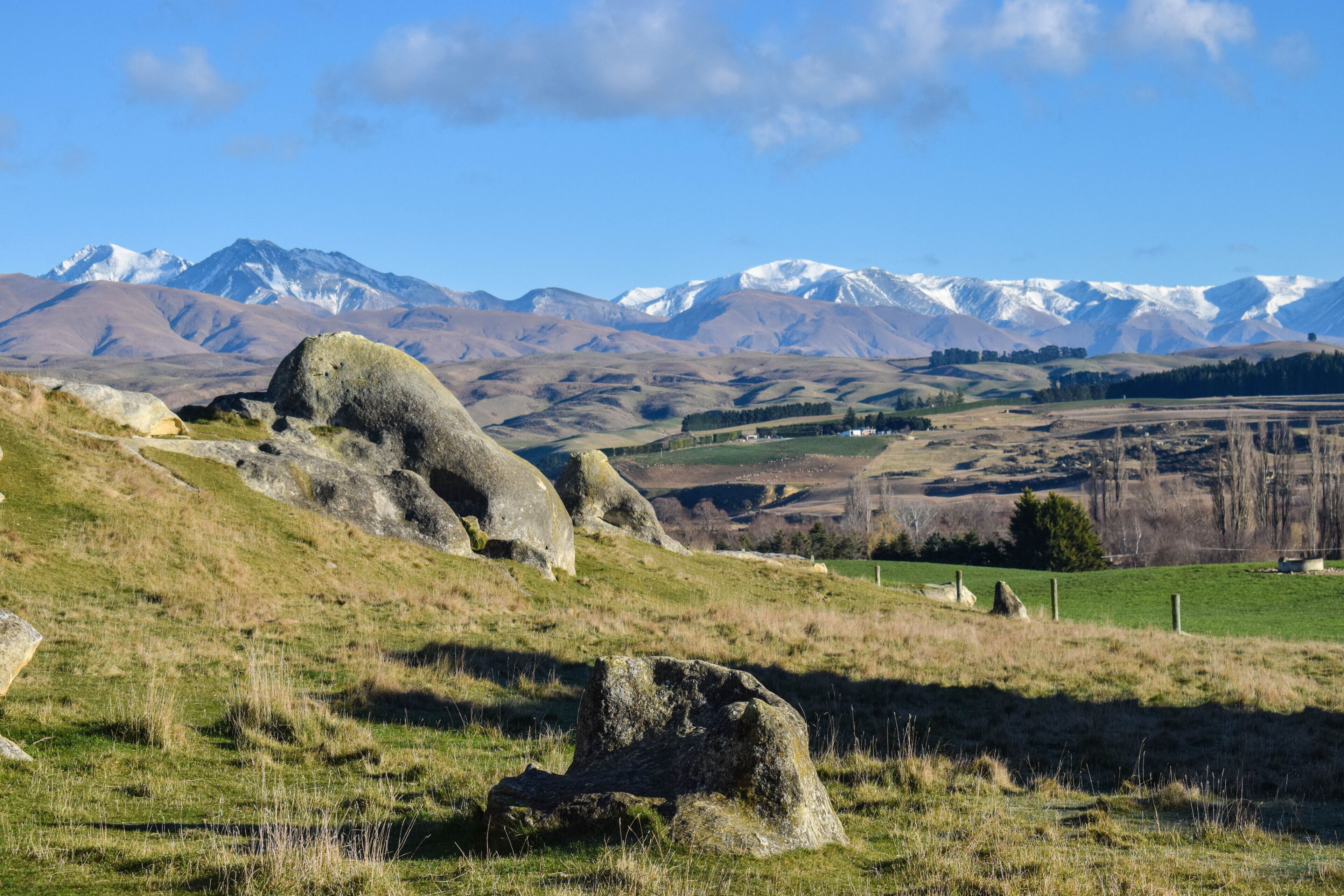 A mountainous landscape with large boulders and a clear view of snow-capped peaks in the distance.