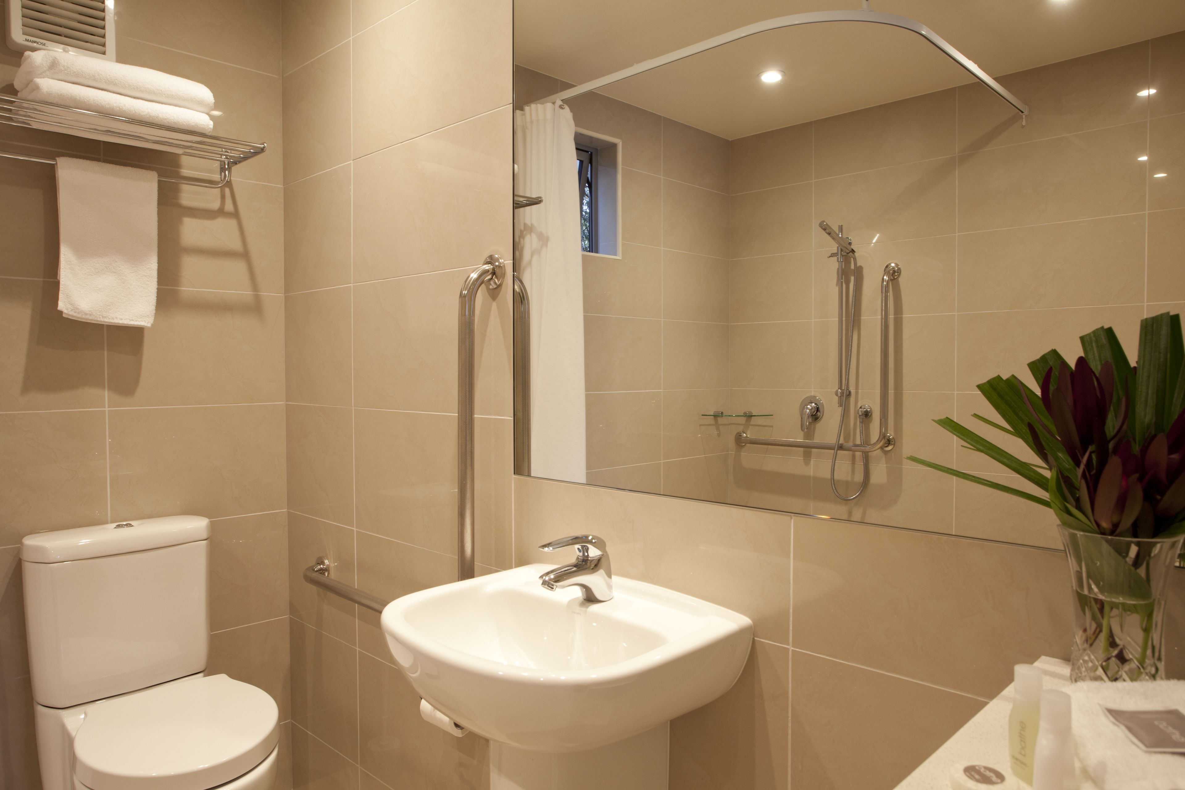 A modern bathroom with a toilet, sink, shower, and a mirror.