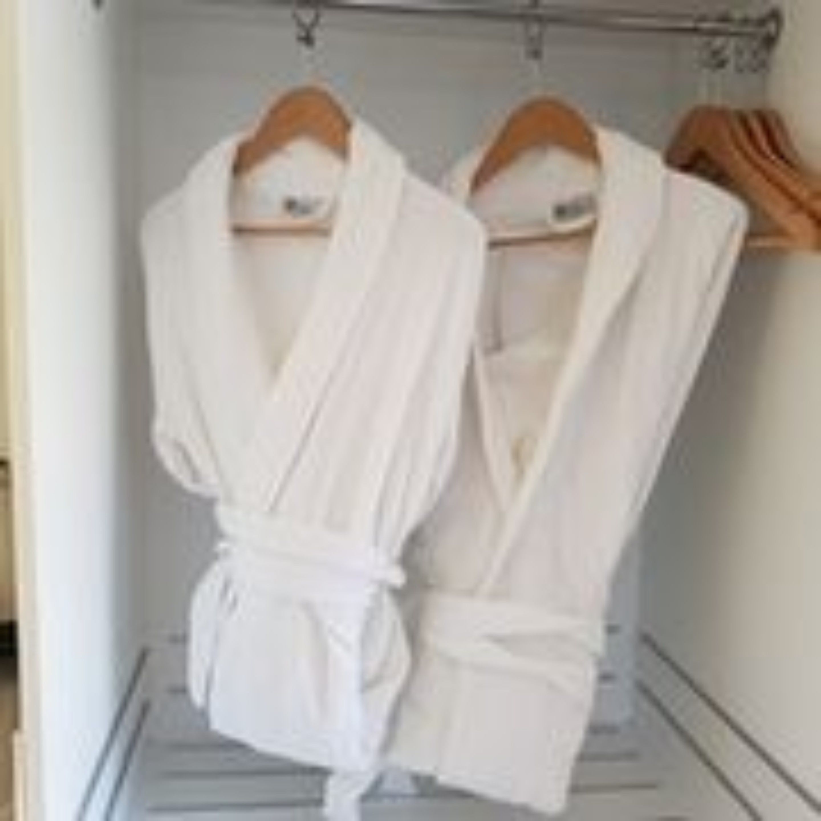 A walk-in closet with two white robes hanging on wooden hangers.