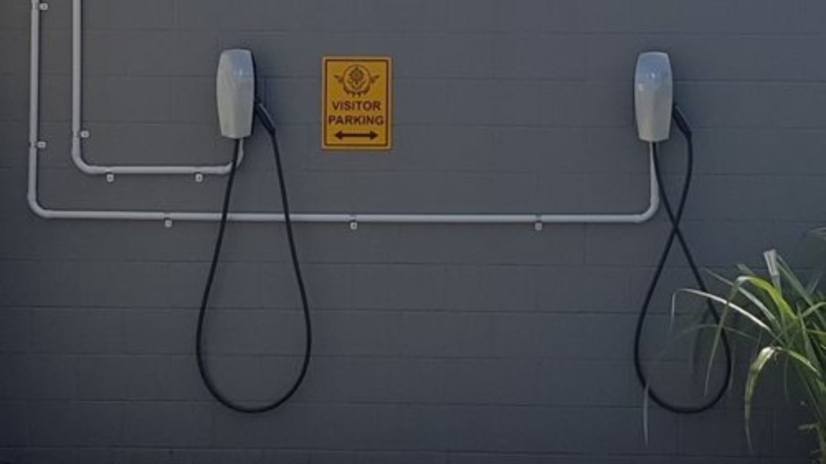 Señal de estacionamiento para visitantes sobre una pared gris, con dos teléfonos conectados por un cable.