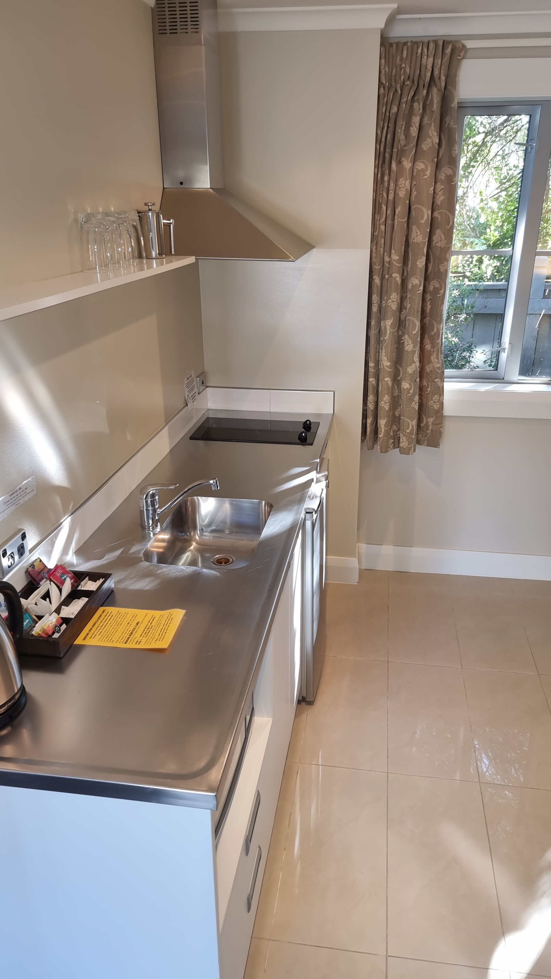 A modern kitchen with a stainless steel sink, a built-in oven, and a window with curtains.