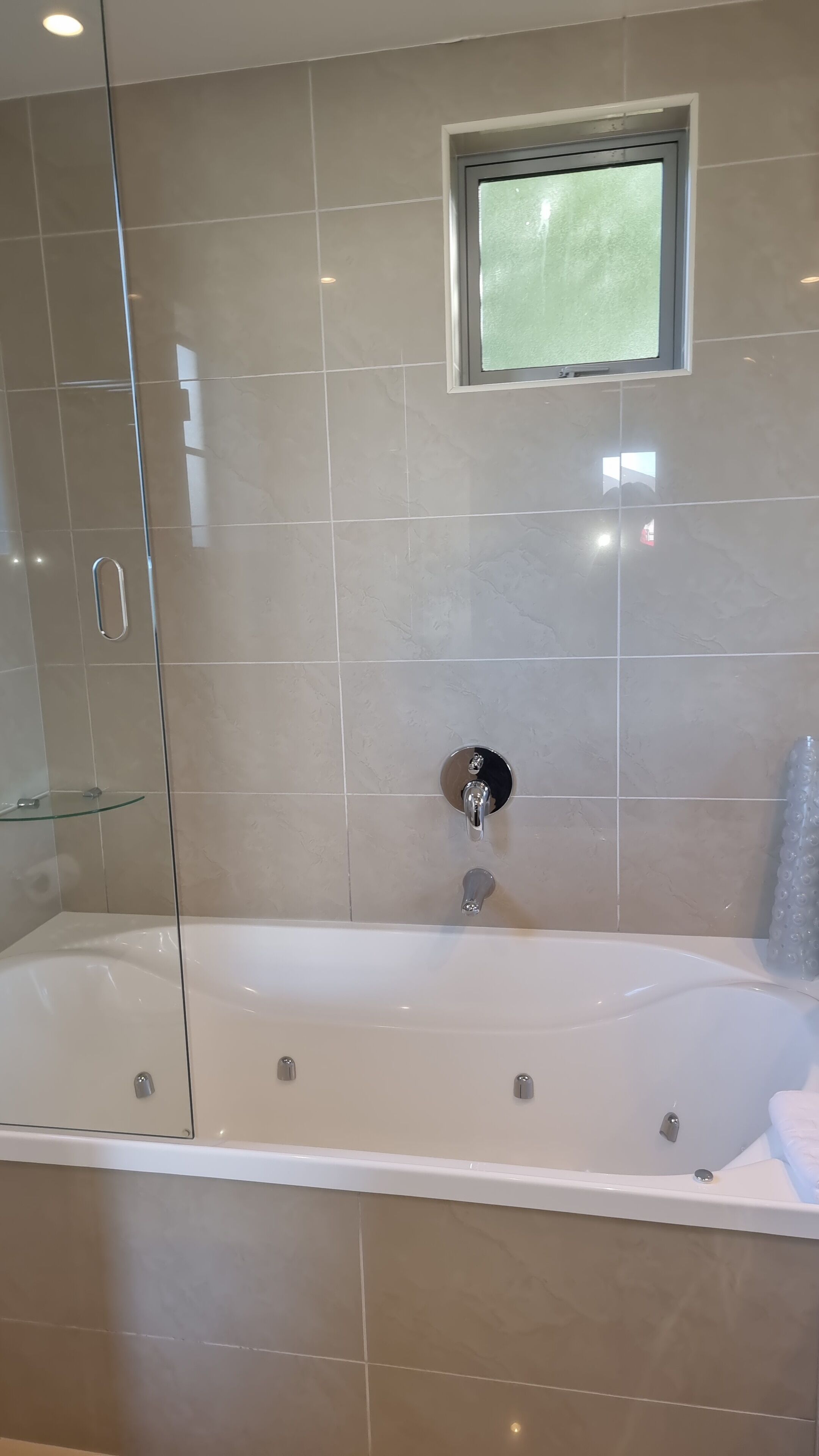 A modern bathroom with a glass-enclosed shower, a large bathtub, and a small window above the tub.