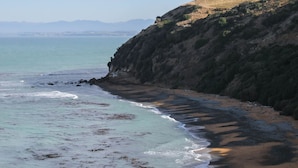 Un paisaje costero con una playa, acantilados rocosos y una vista distante de montañas.