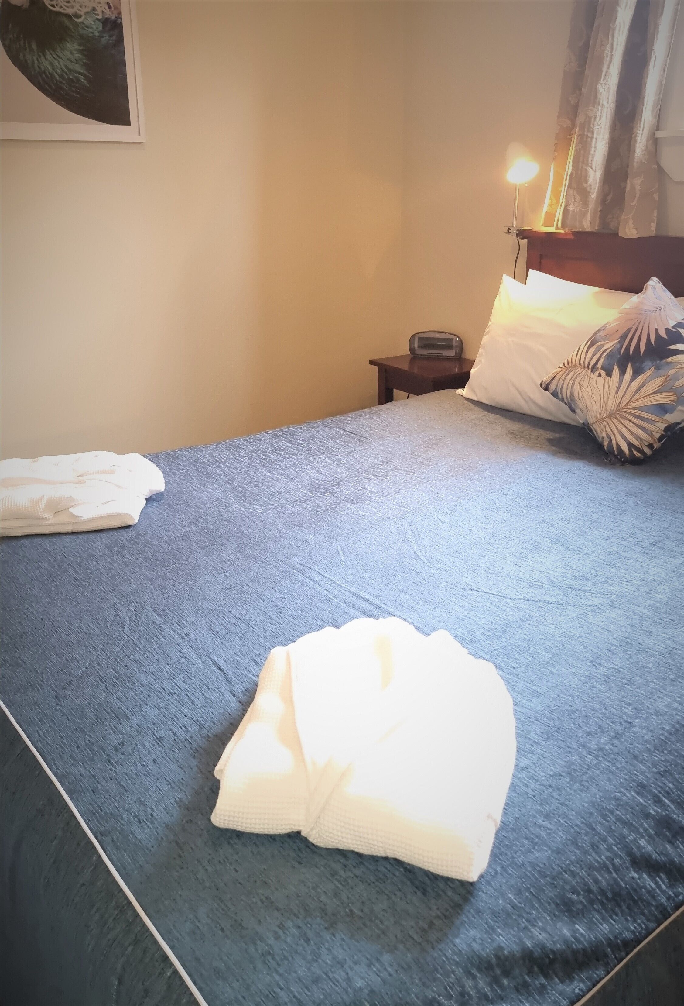 A neatly made bed with a blue bedspread, white pillows, and a folded white towel on the bed.