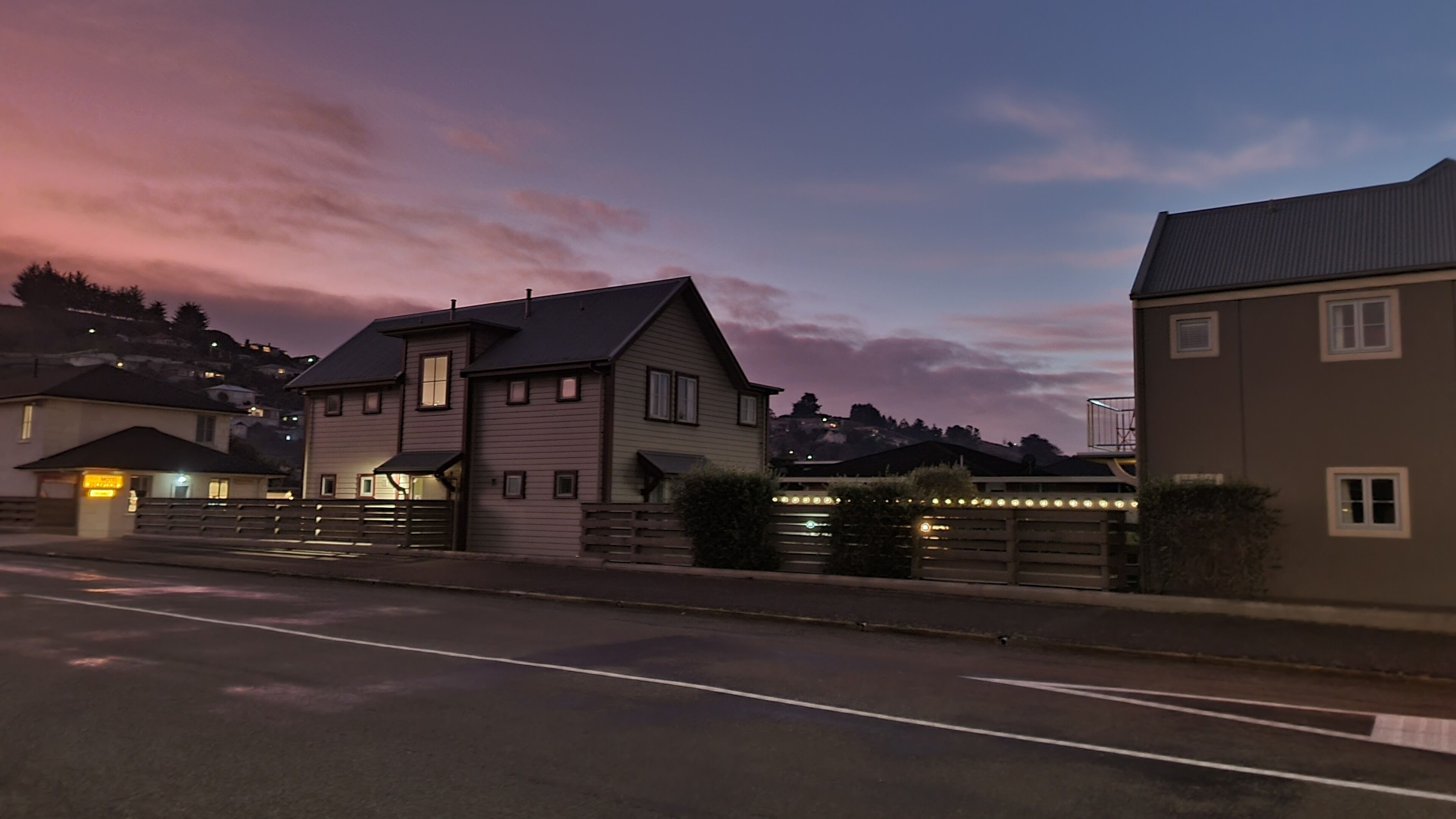 A residential street with houses, a gated entrance, and a clear sky at dusk.