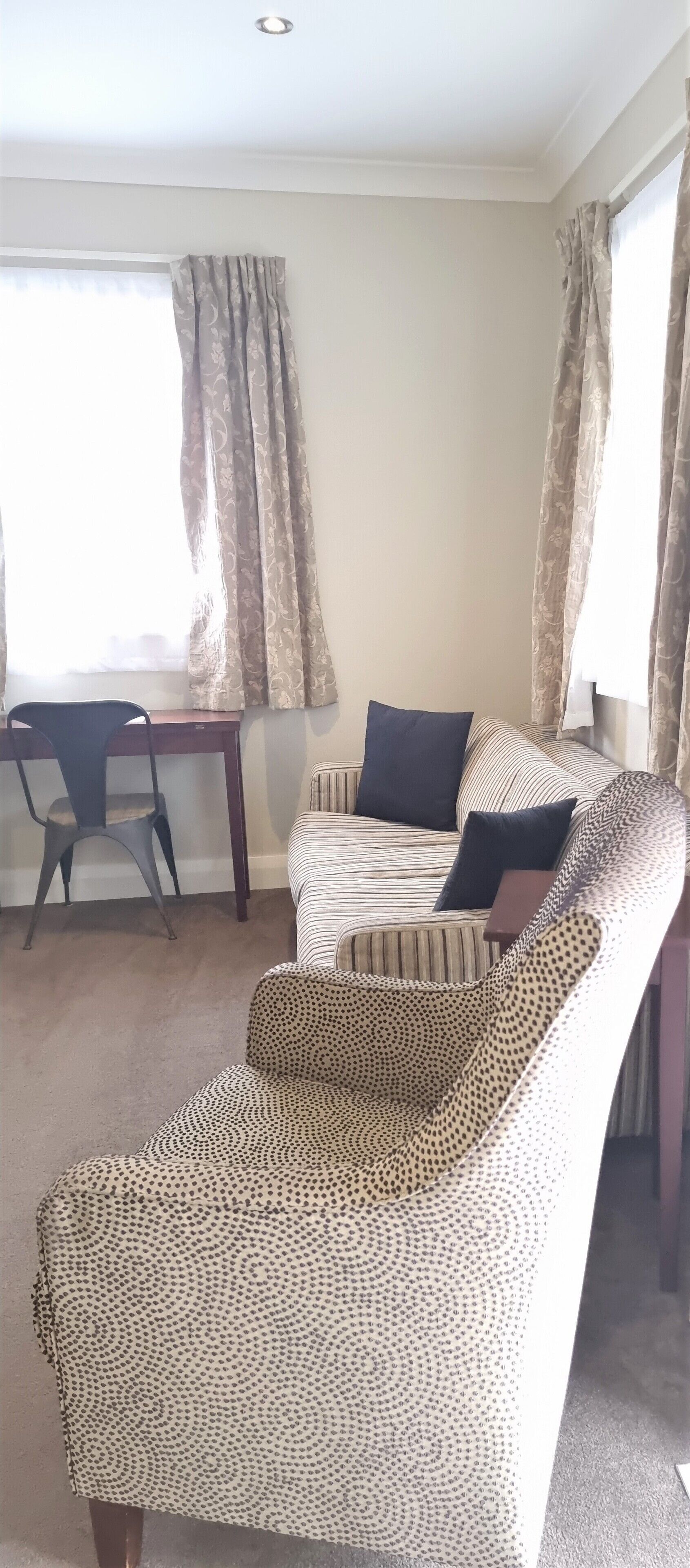 A living room with a striped sofa, a leopard print armchair, a wooden desk, and a chair.