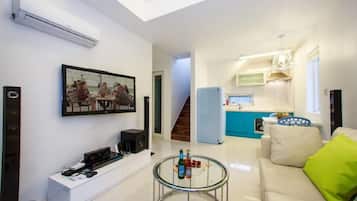 A modern living room with a glass coffee table, a sofa, and a dining area with a painting.