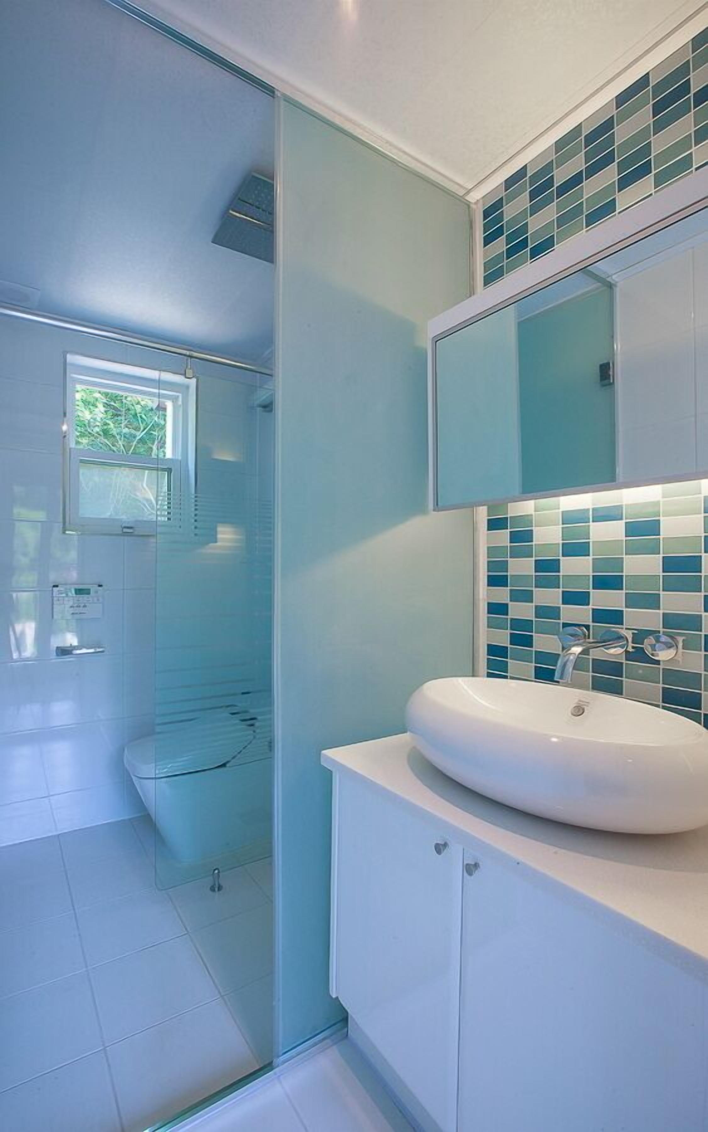 Une salle de bain moderne avec une douche à parois de verre, un lavabo blanc et un mur recouvert de carreaux.