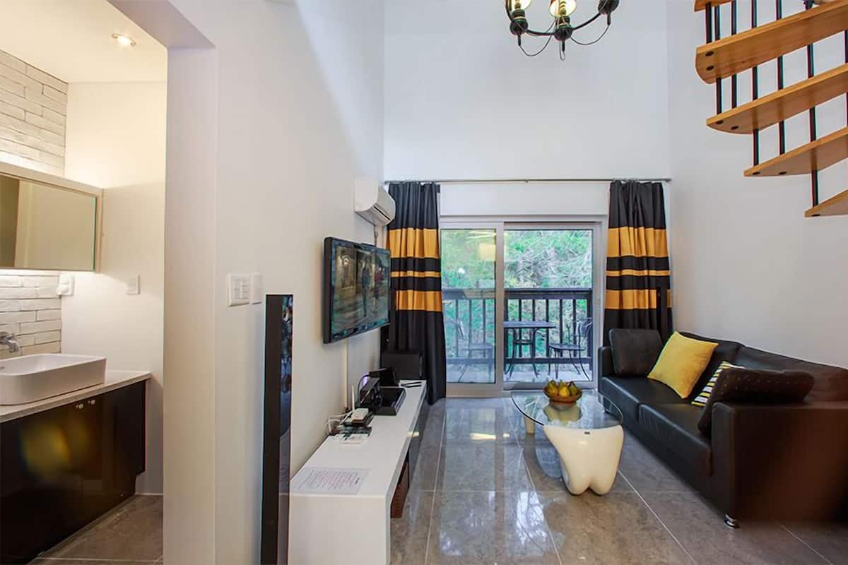 A modern living room with a sofa, a coffee table, a TV, and a staircase.