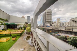 Eine Dachterrasse mit Blumentöpfen und Blick auf eine Stadtlandschaft, einschließlich hoher Gebäude und einer Brücke.