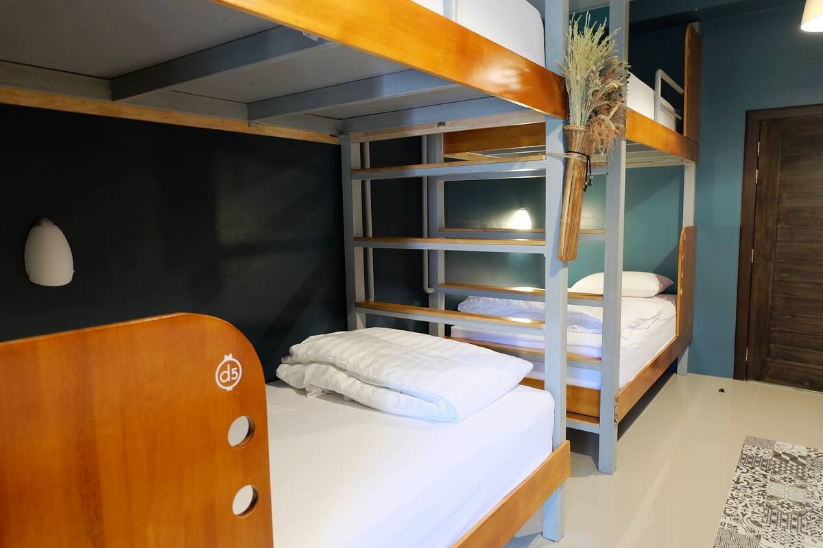 A bunk bed with a wooden headboard, a bedside table, and a wall-mounted shelf with a vase of dried plants.