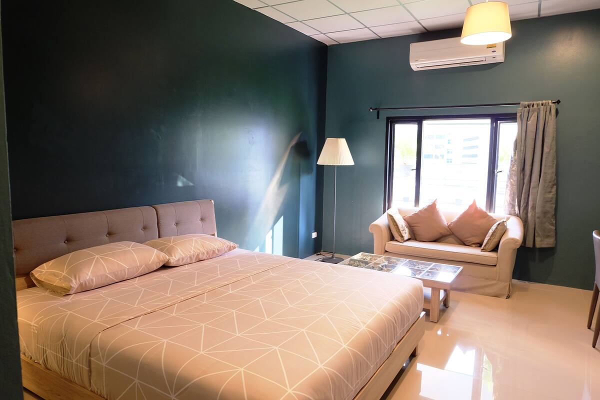 A bedroom with a large bed, a sofa, a lamp, and a window.
