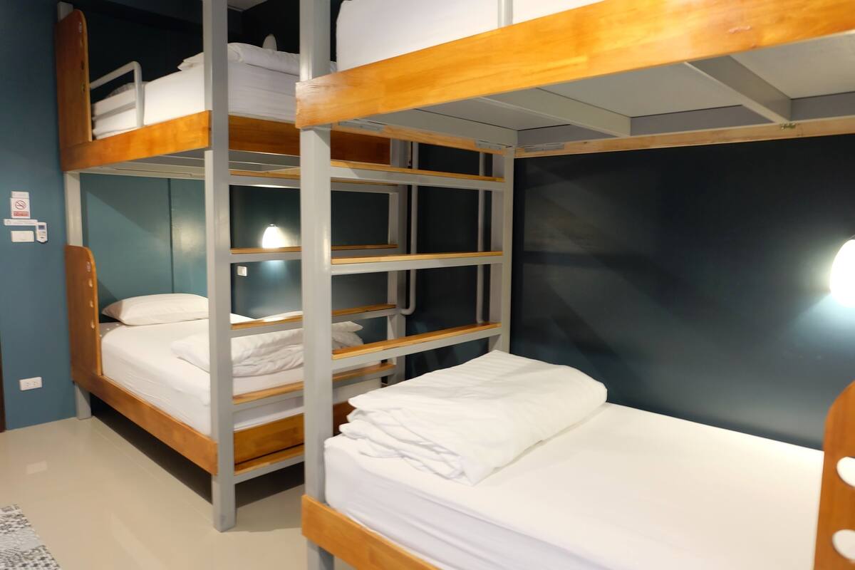 A bunk bed room with a wooden frame, white bedding, and a wall-mounted light.