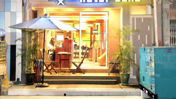 Un hotel con una insegna che recita "hotel bond", caratterizzato da un motivo a scacchi sulla facciata, balconi con ringhiere in metallo e un ingresso ben illuminato.
