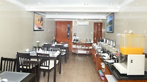 Un'area ristorazione in hotel con tavoli, sedie e un banco buffet con cibo e bevande.