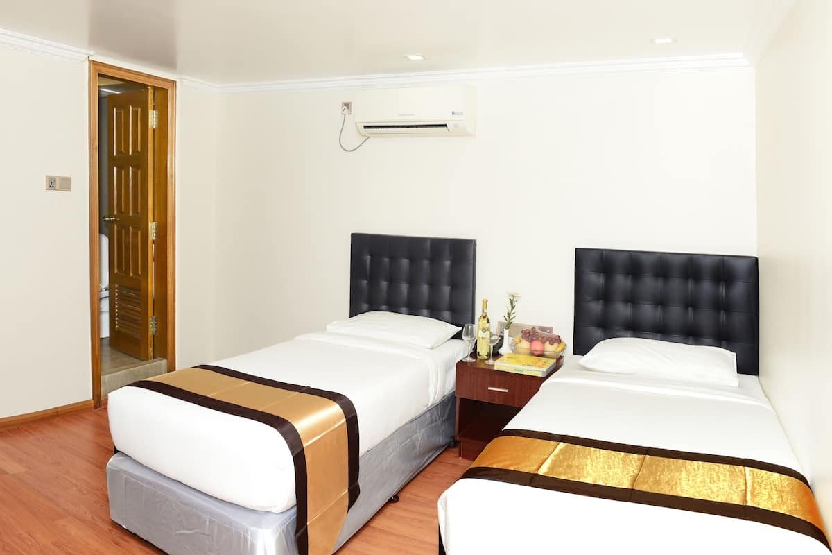 A hotel room with two beds, a wooden door, an air conditioning unit, and a bedside table with a bottle and flowers.