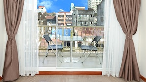 Un balcone con tavolo e sedie, vista su edifici e tende marroni.