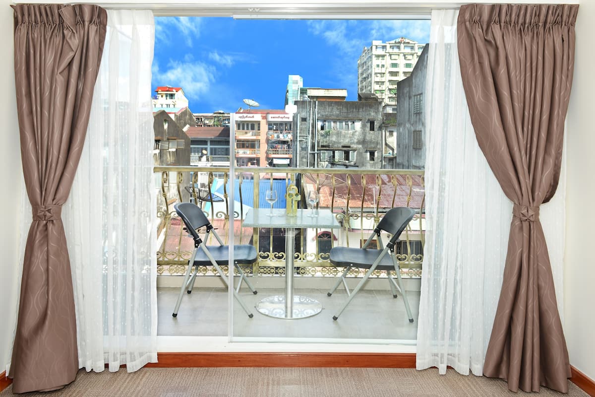 A balcony with a table and chairs, a view of buildings, and brown curtains.