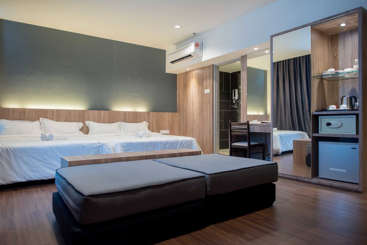 Quarto de hotel moderno com duas camas, cabeceira de madeira, um espelho grande, escrivaninha e um minibar.