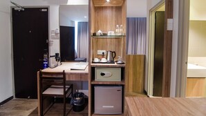 A compact hotel room with a wooden desk, a small refrigerator, a chair, a trash bin, and a shelf with toiletries. - Mornington Hotel Soon Choon (Ipoh)