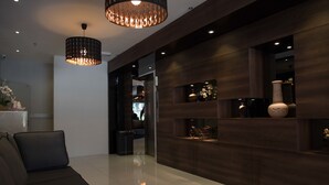 A modern living room with a dark brown sofa, a large wooden wall unit with decorative items, and a hanging light fixture. - Mornington Hotel Soon Choon (Ipoh)