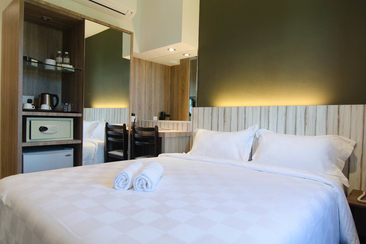 Quarto de hotel com cama bem arrumada, uma pequena mesa com cafeteira e uma cadeira.