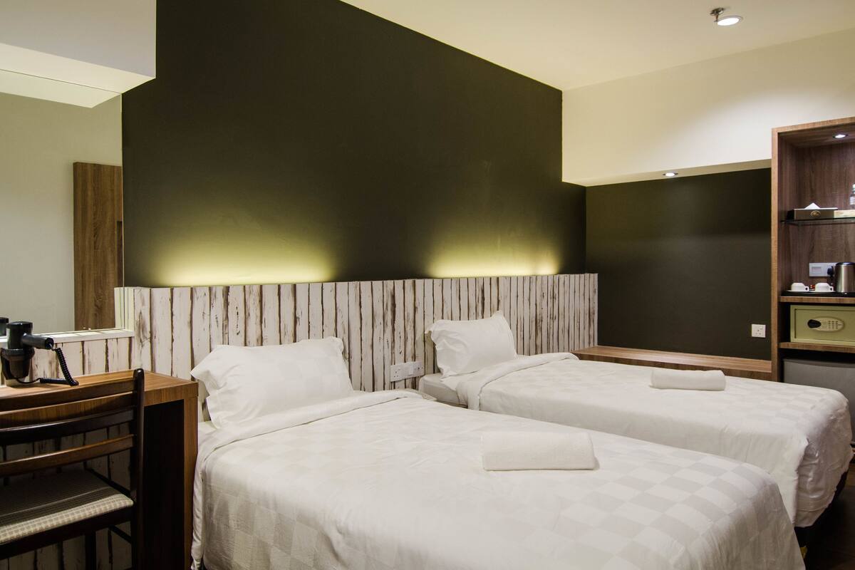 Quarto de hotel com duas camas, uma escrivaninha com cadeira e uma pequena cozinha.