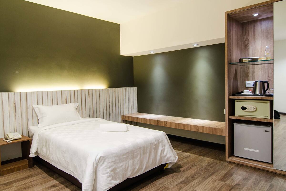 Quarto de hotel moderno com cama, mesa de cabeceira e mini-bar embutido.