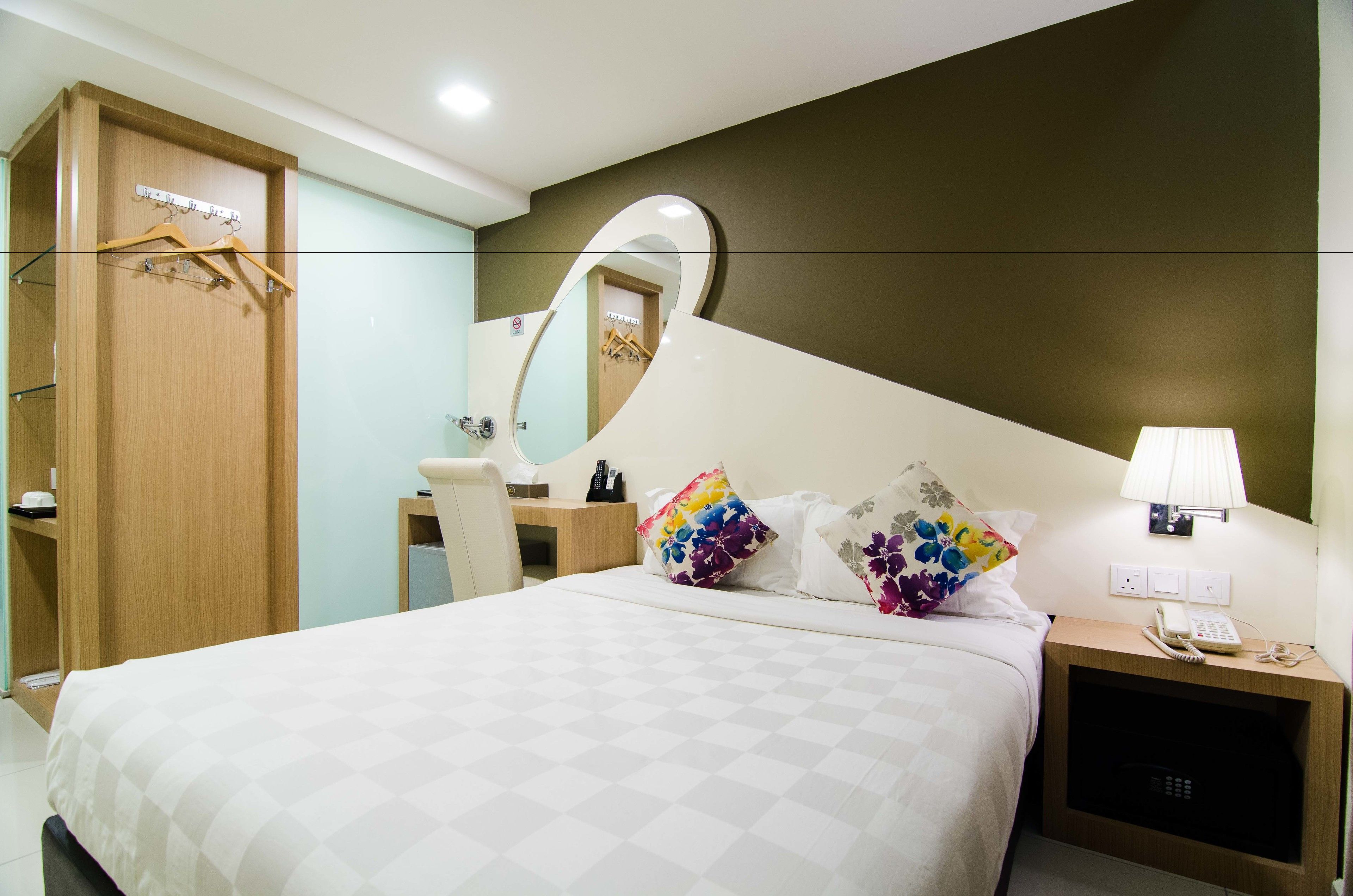 A hotel room with a bed, bedside table, lamp, and a mirror.