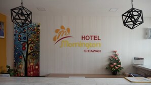 Una zona de recepció amb un quadre abstracte i colorit, un logotip de HOTEL Mornington Siti Awan, i una taula de recepció amb un ram de flors.