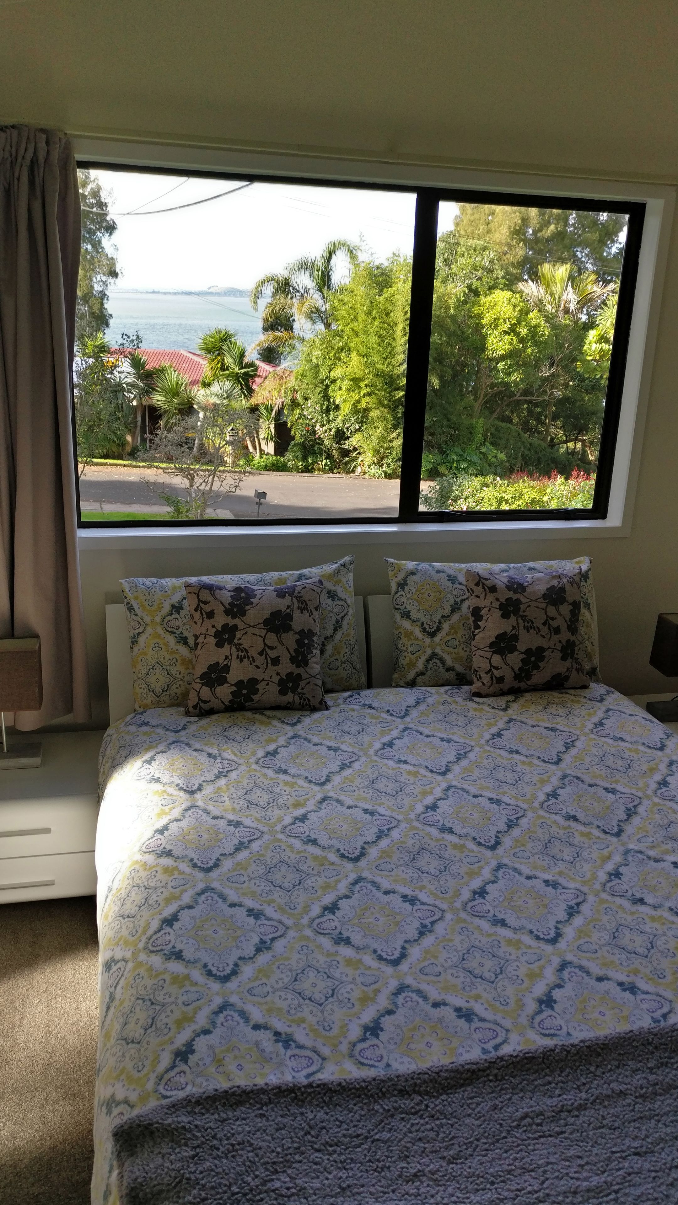 A bedroom with a bed, two pillows, a window, and a view of a body of water and greenery.