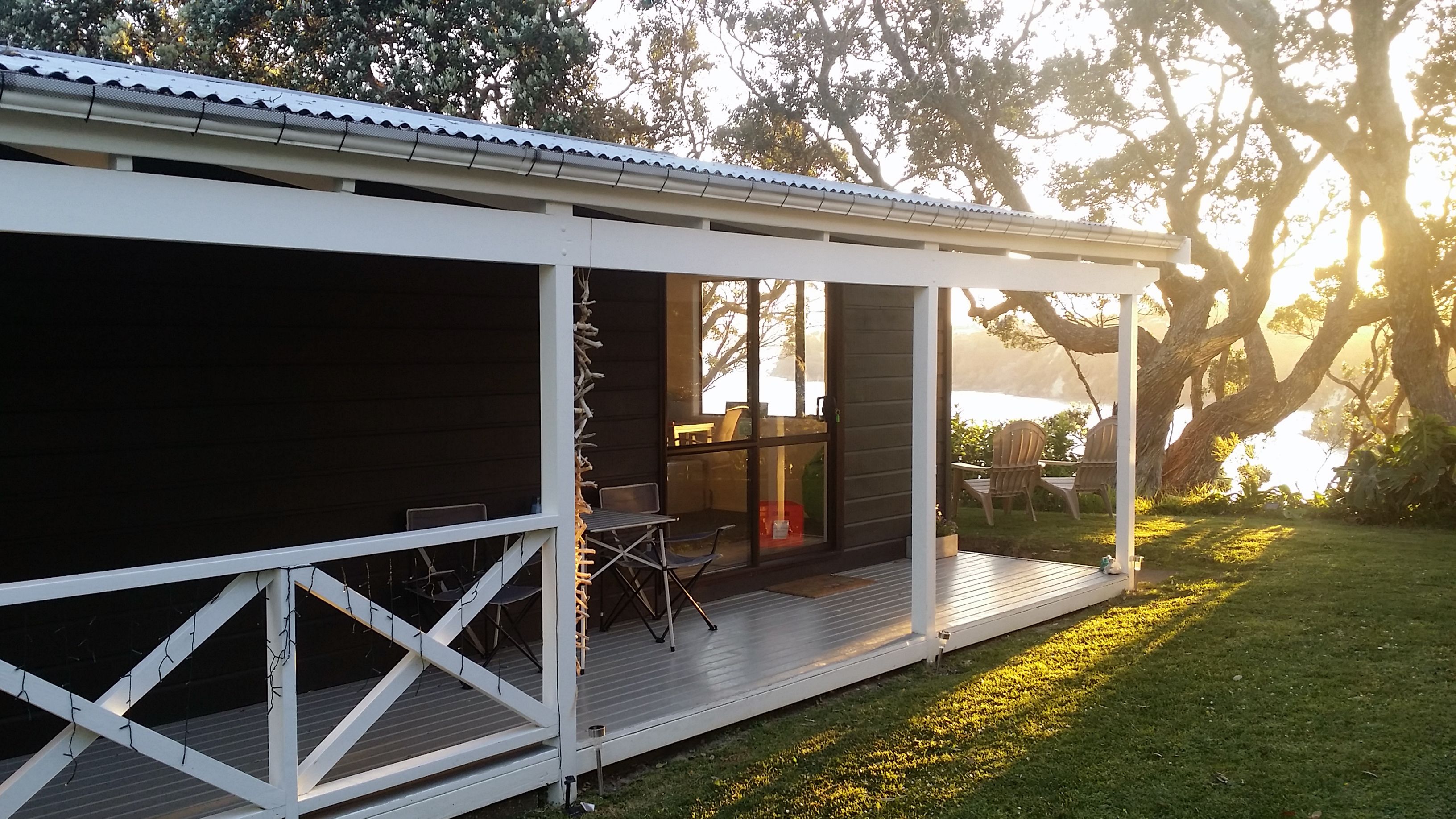 A covered outdoor area with a wooden deck, a seating area with chairs, and a view of a body of water in the background.