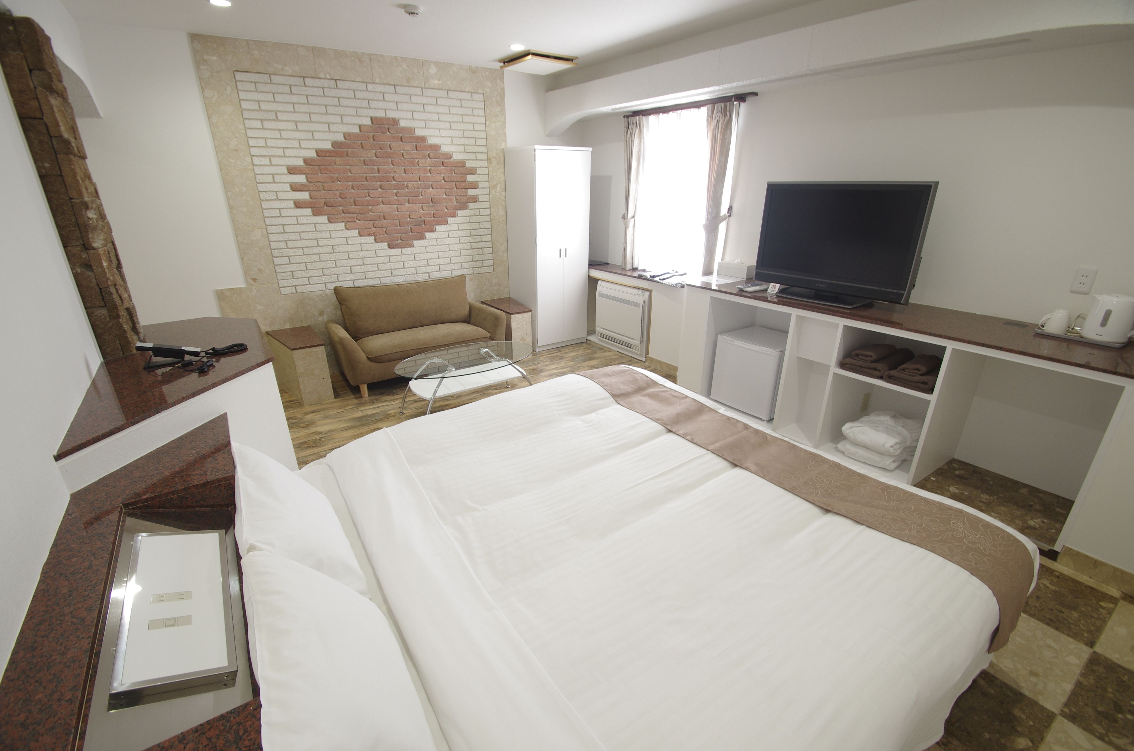 A hotel room with a bed, a TV, a sofa, a desk, and a brick-patterned wall.