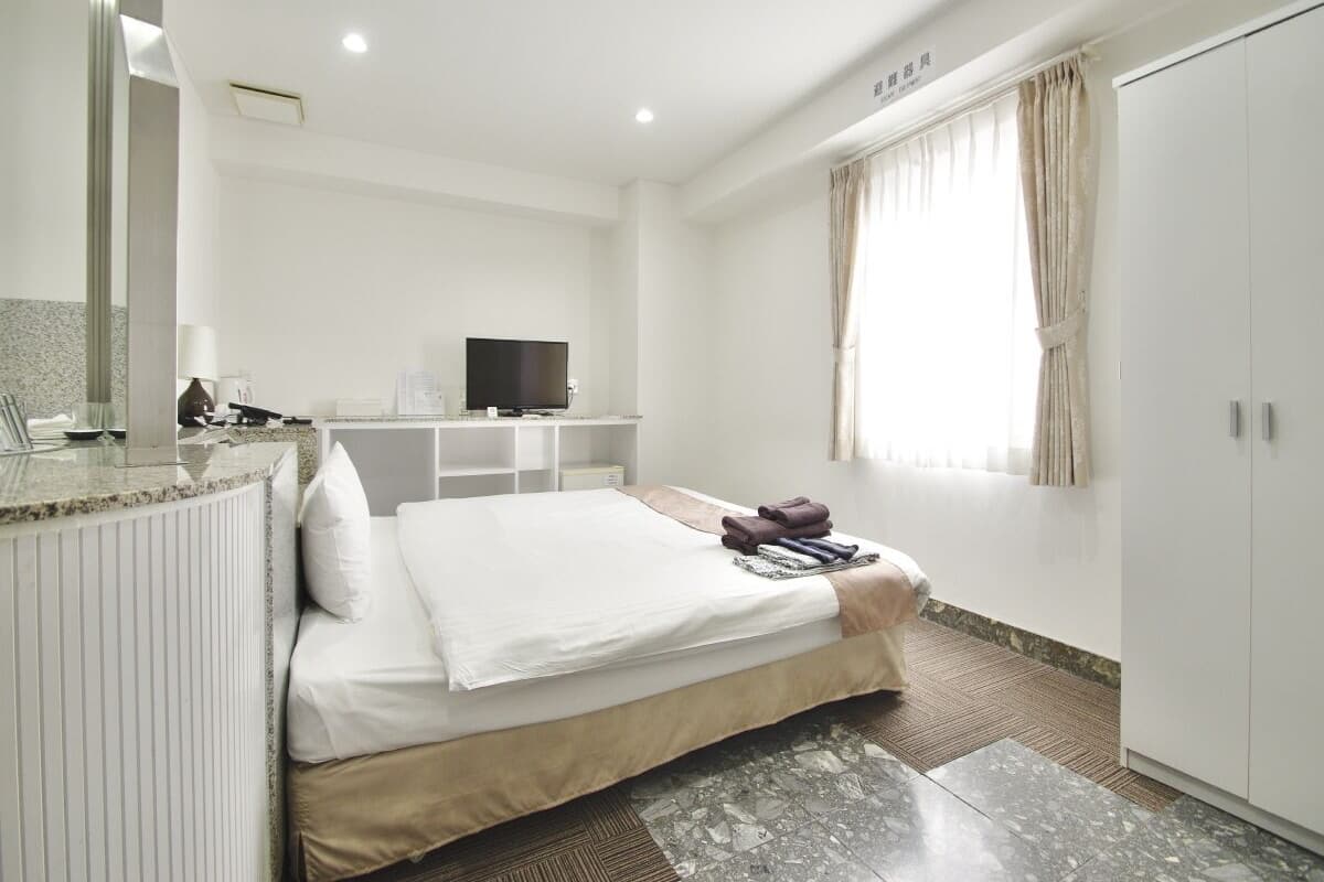 Una camera d'albergo con un letto, una televisione, una scrivania e un armadio.