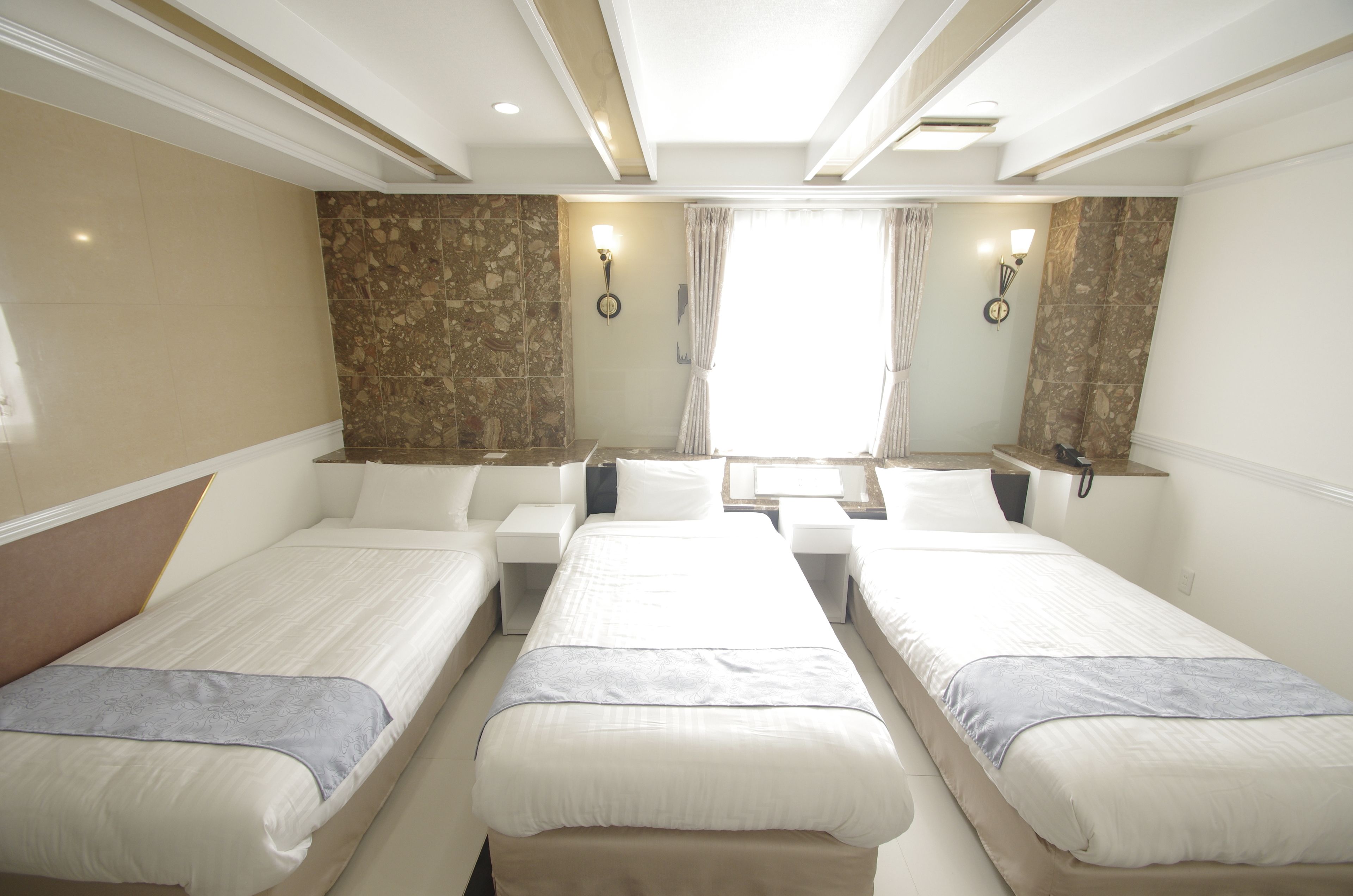 A hotel room with two single beds, a small table, and a nightstand with a lamp.