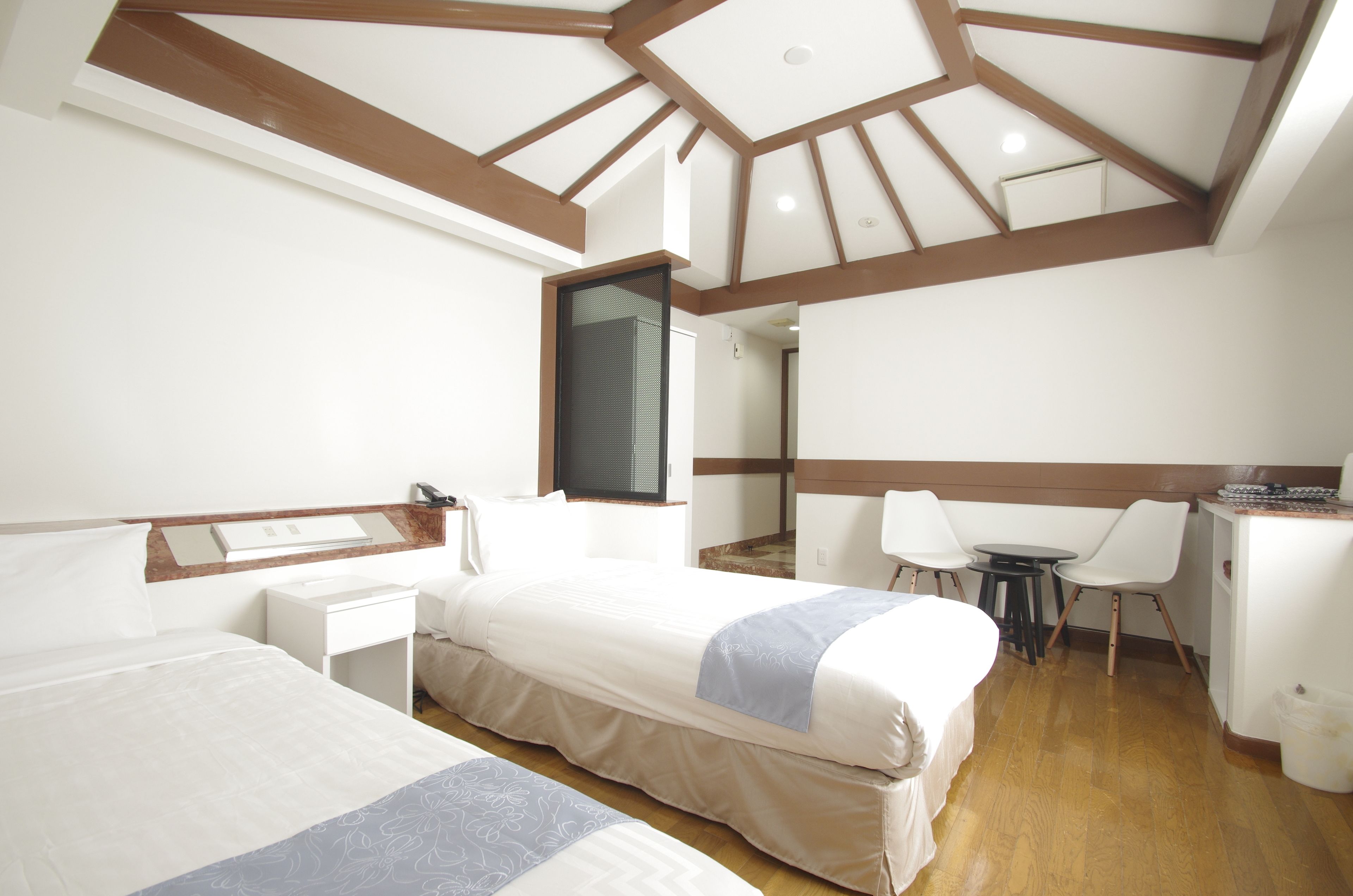 A hotel room with two beds, a desk, a chair, a small table, and a TV.