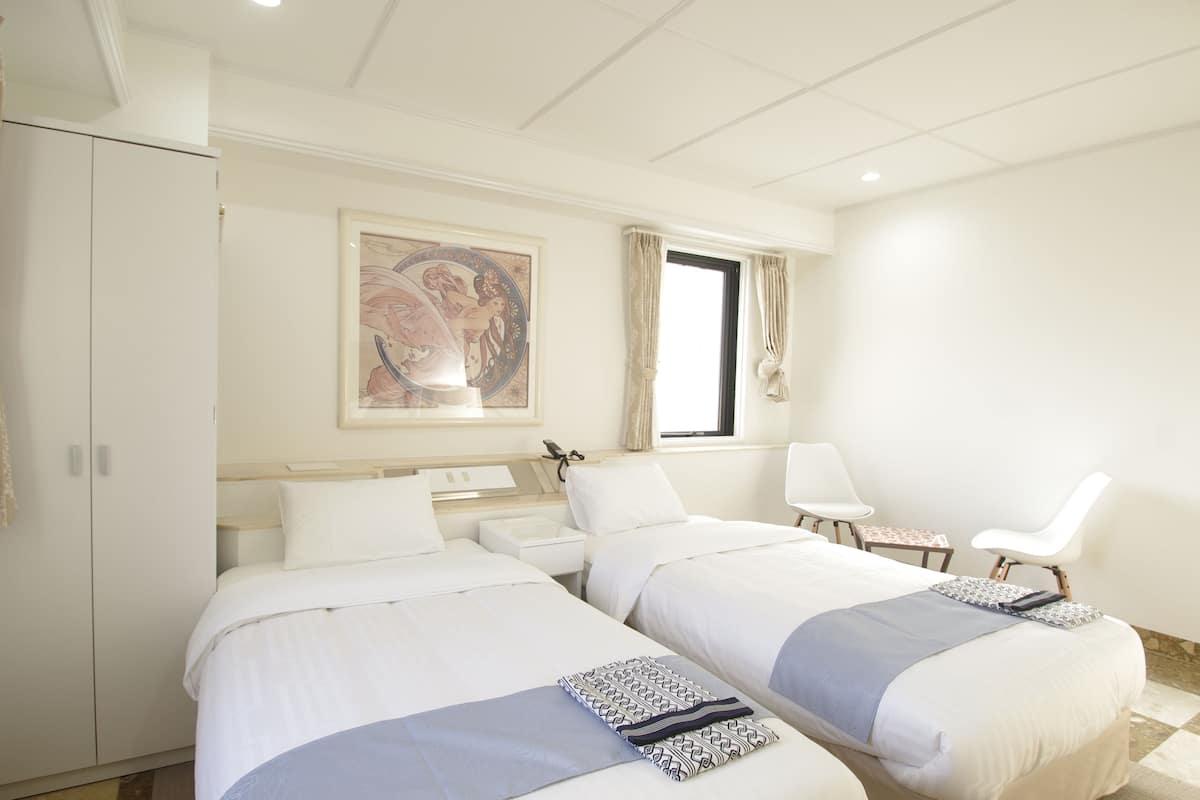 Camera d'albergo con due letti, una scrivania, una sedia e una finestra con tende.