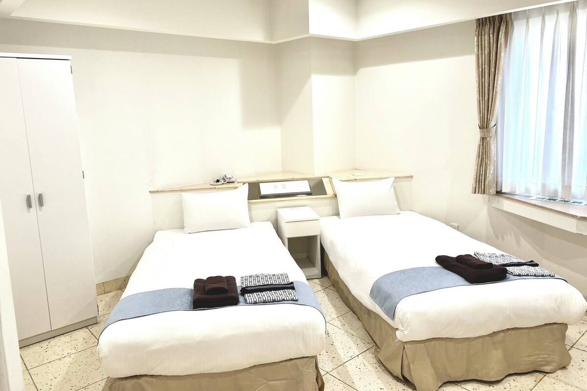 Una camera d'albergo con due letti singoli, una scrivania, un armadio e una finestra con tende.