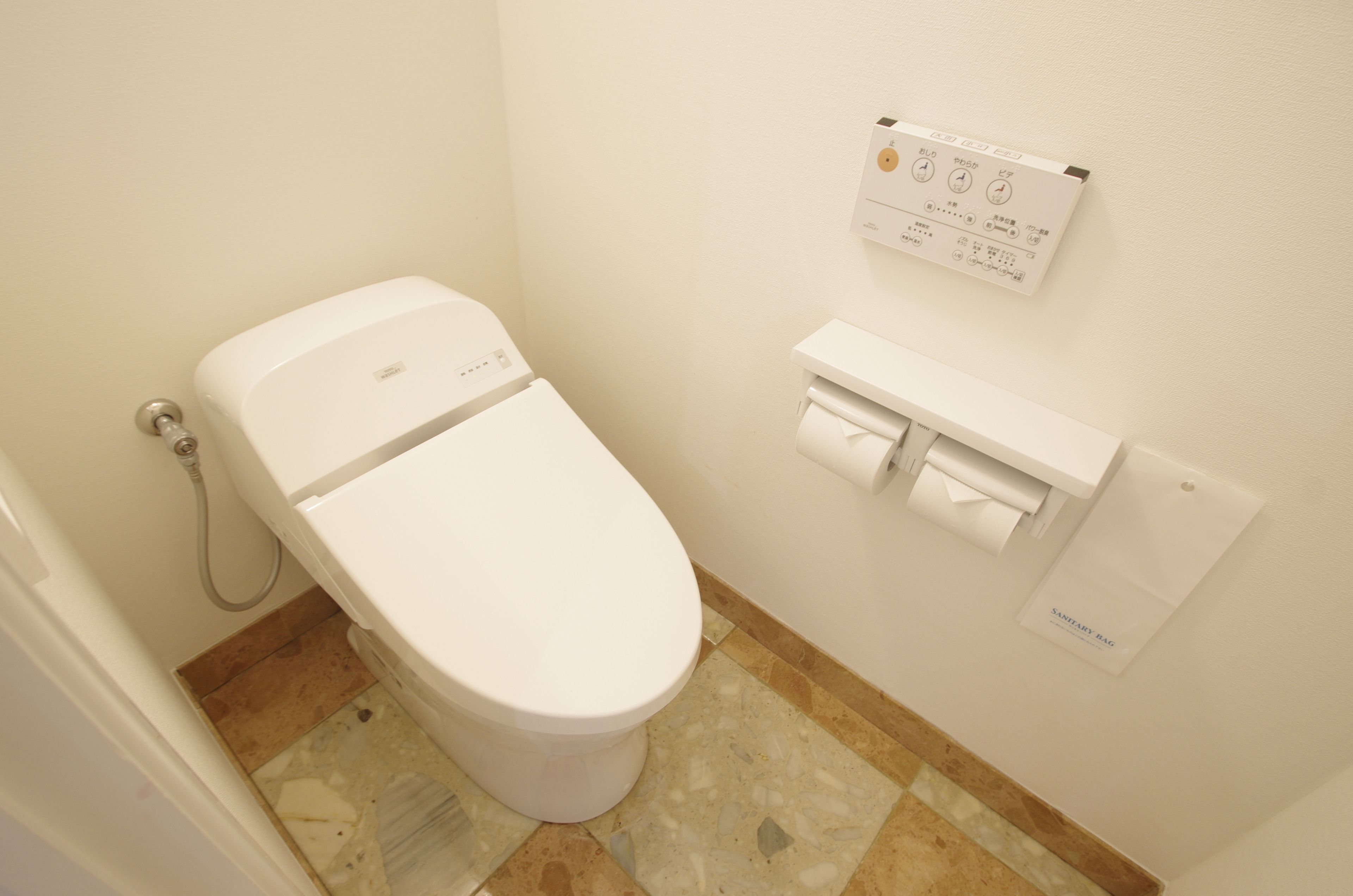 A white toilet with a control panel above it, a paper towel dispenser, and a hand dryer on the wall.