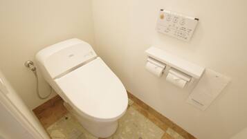 A white toilet with a control panel above it, a paper towel dispenser, and a hand dryer on the wall.