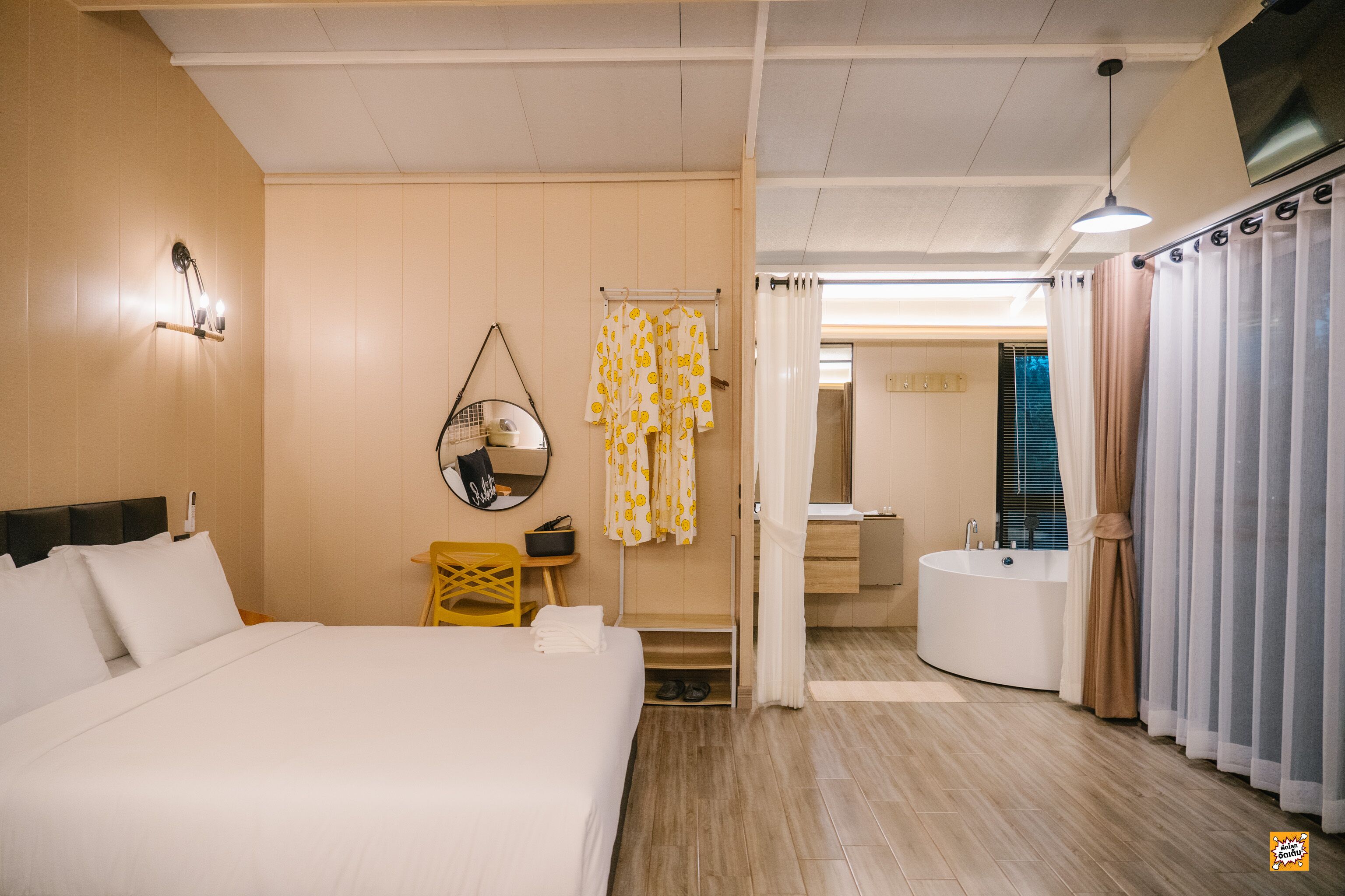 Quarto de hotel com uma cama grande, uma mesinha, uma cadeira, um espelho, banheiro com banheira e chuveiro.