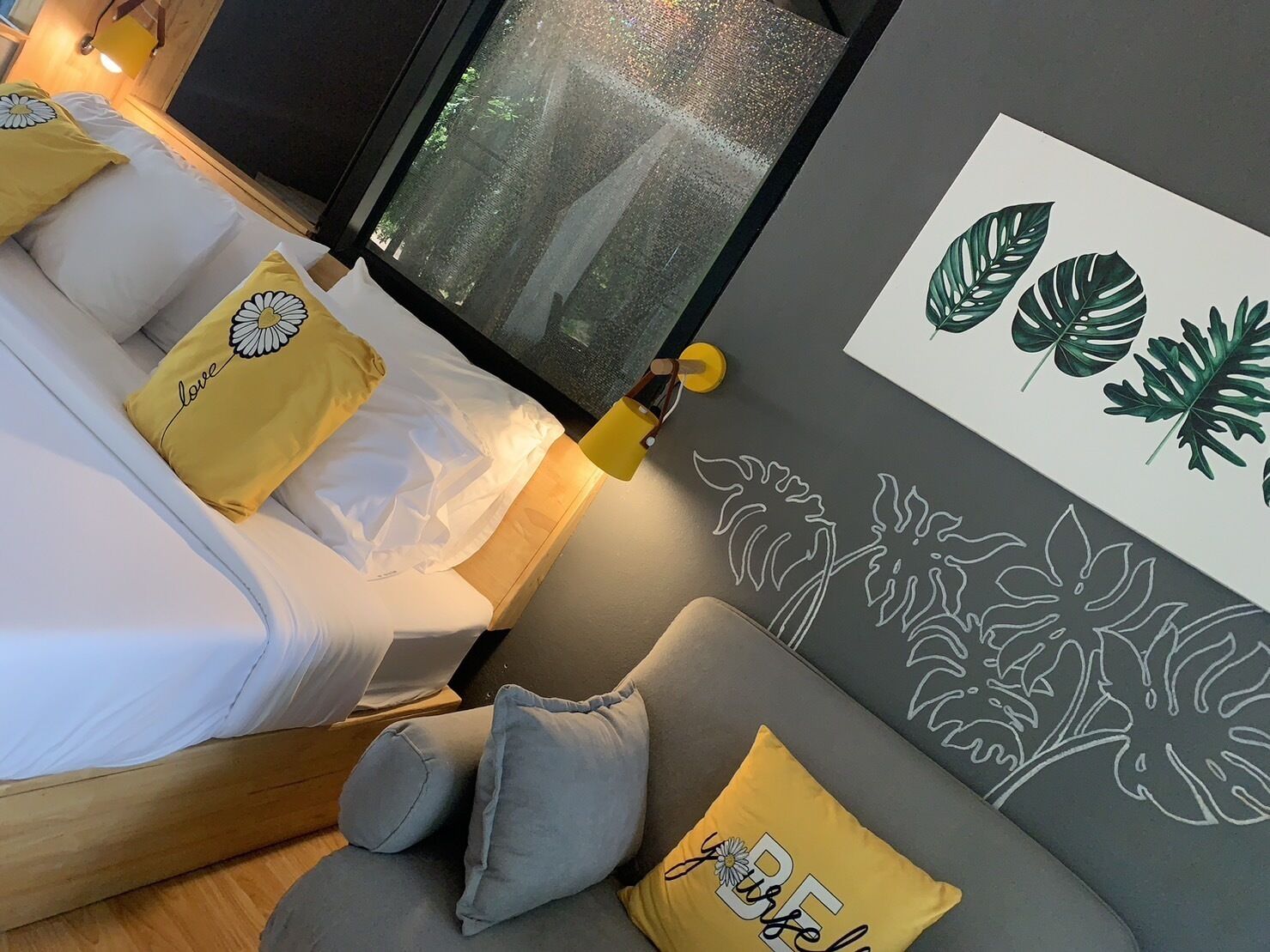 A cozy bedroom with a bed, a sofa, and a wall with leaf patterns.